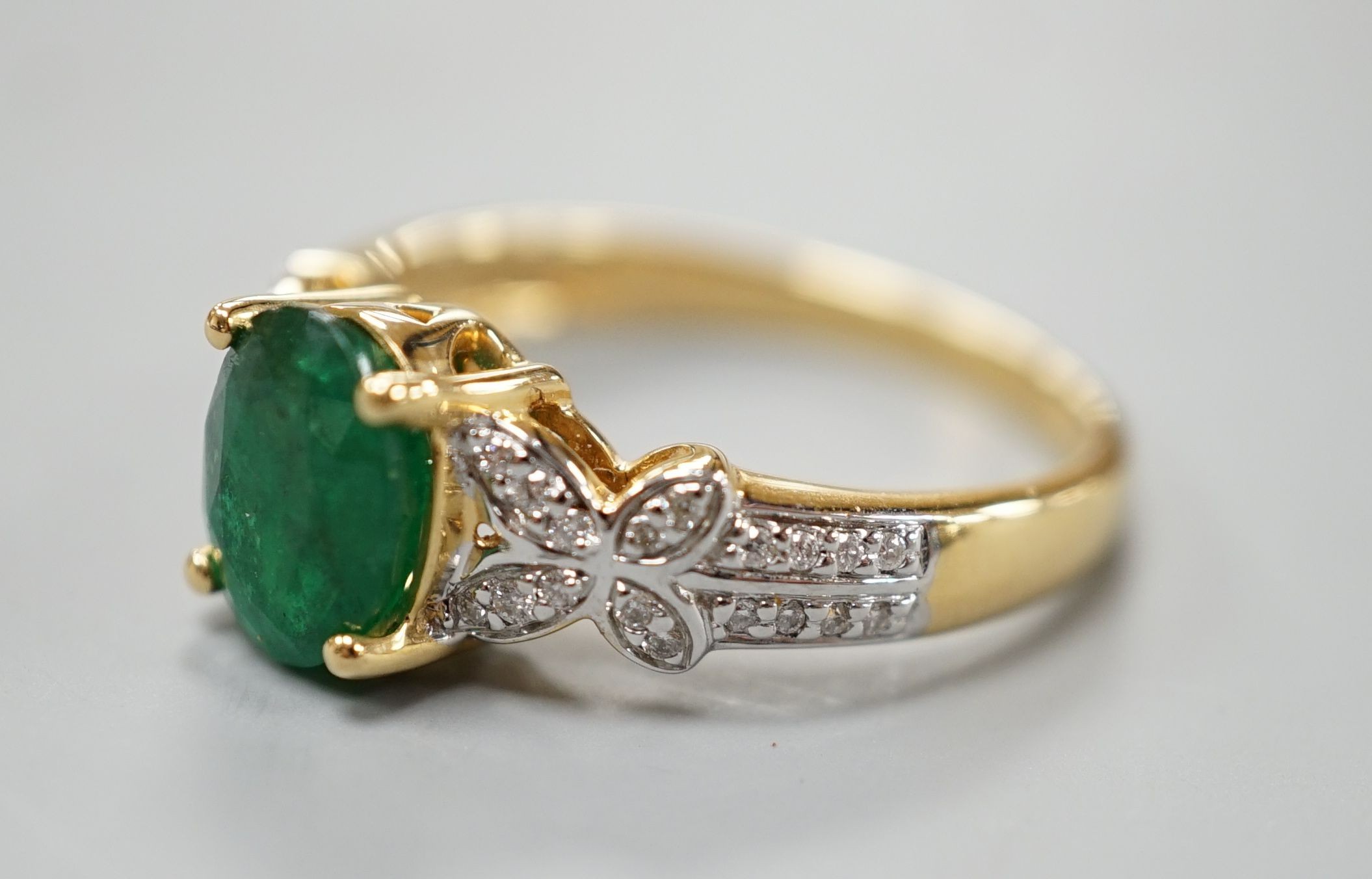 A modern 18ct gold and single stone emerald set dress ring, with diamond chip set shoulders, size R, gross weight 5.5 grams.